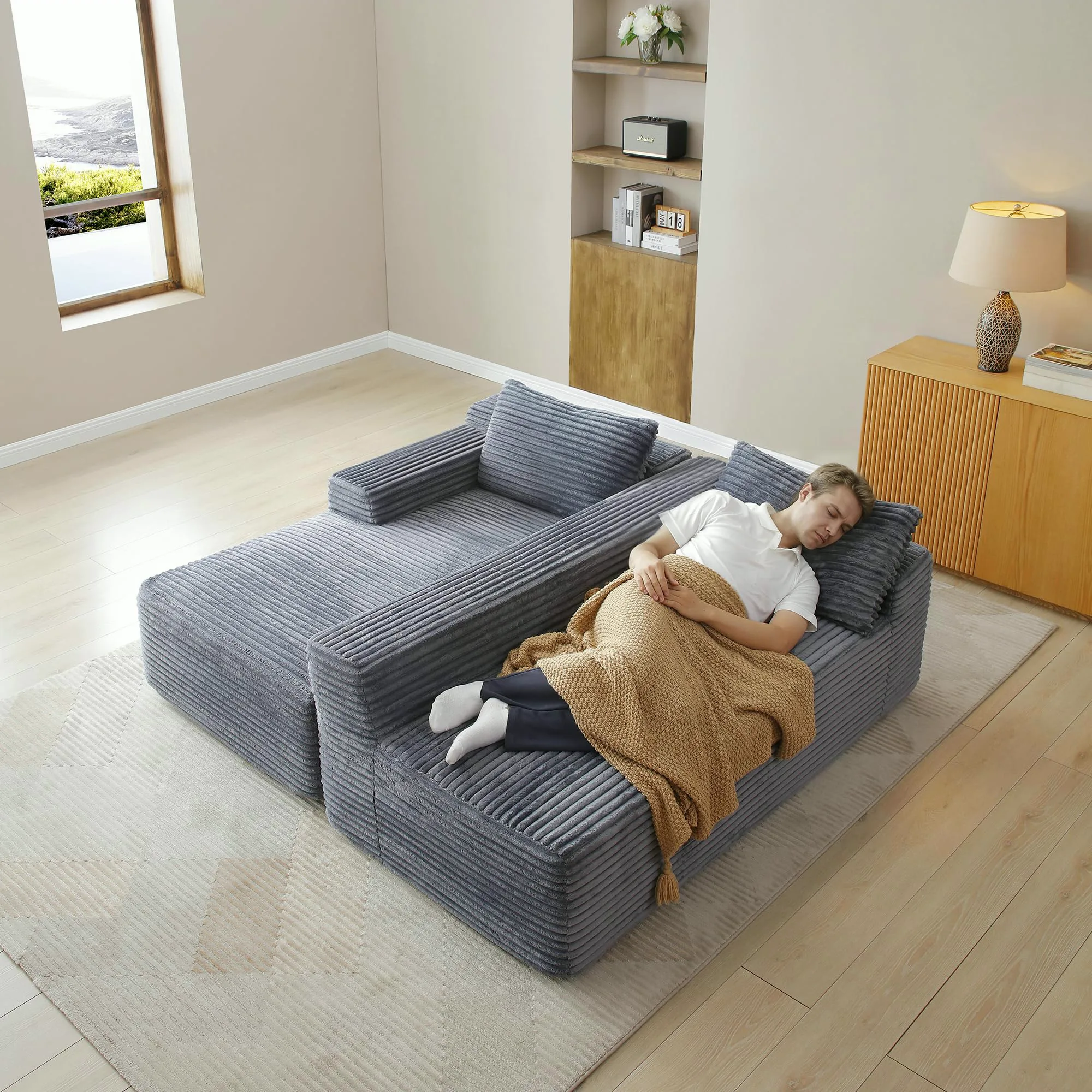 Man lying full length on the chaise of a gray corduroy cloud sectional under a throw